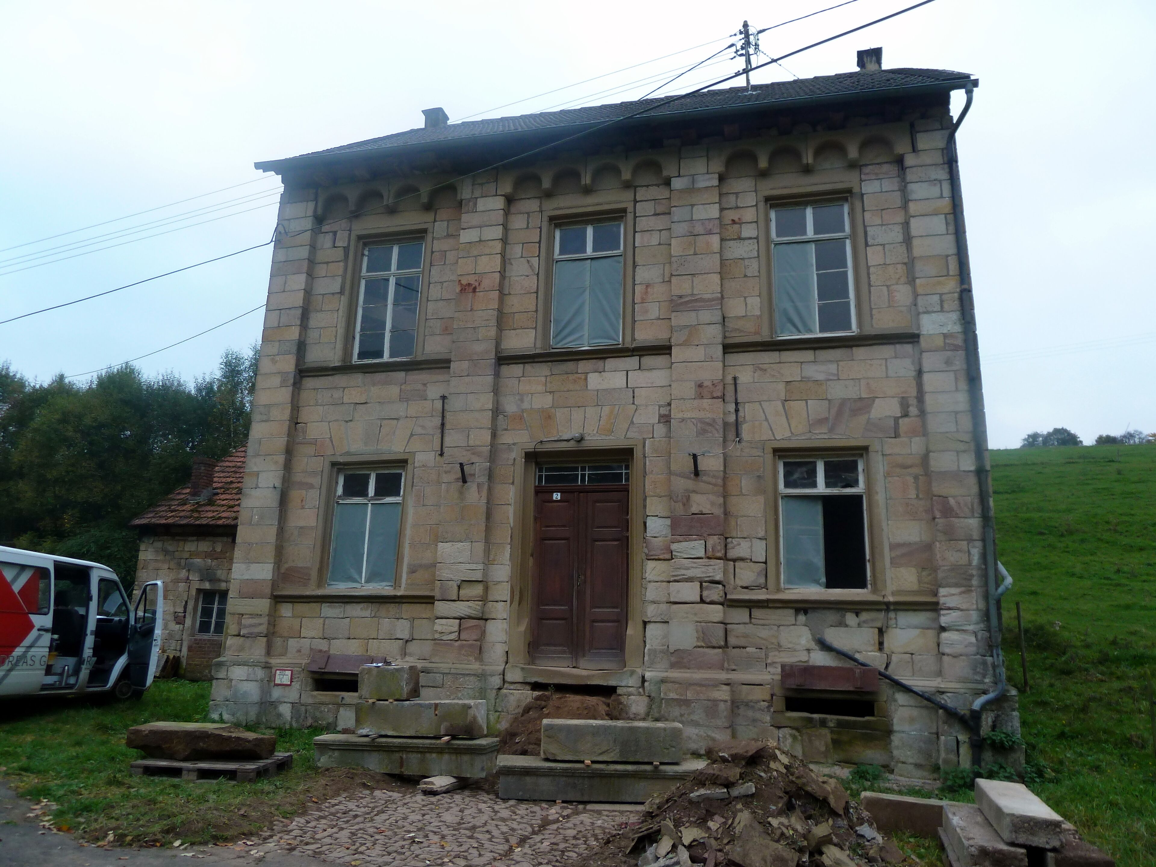 A stone building with a wooden door and windows, surrounded by a grassy area.