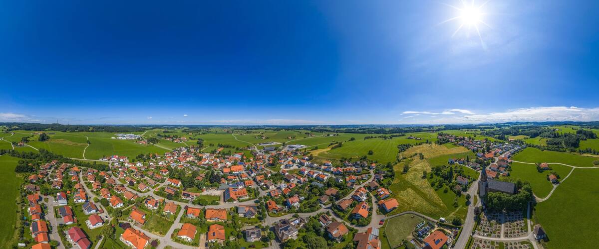 An aerial view of a village with red-roofed houses, green fields, and a church.