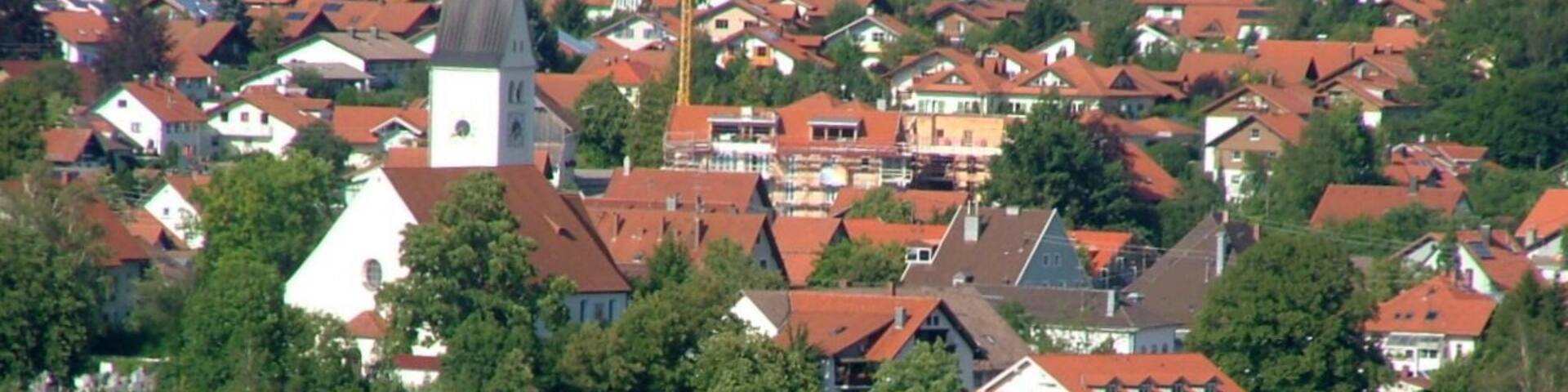 A village with red-roofed houses, a church with a steeple, and surrounding green fields.