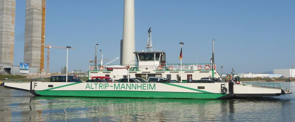 A ferry named ALTRIP-MANNHEIM docked at a port with industrial buildings and cranes in the background.