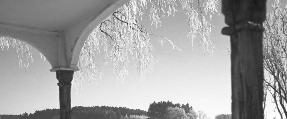 A snow-covered landscape with a gazebo and bare trees.