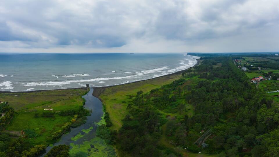 A coastal landscape with a river, dense forest, and a beach.