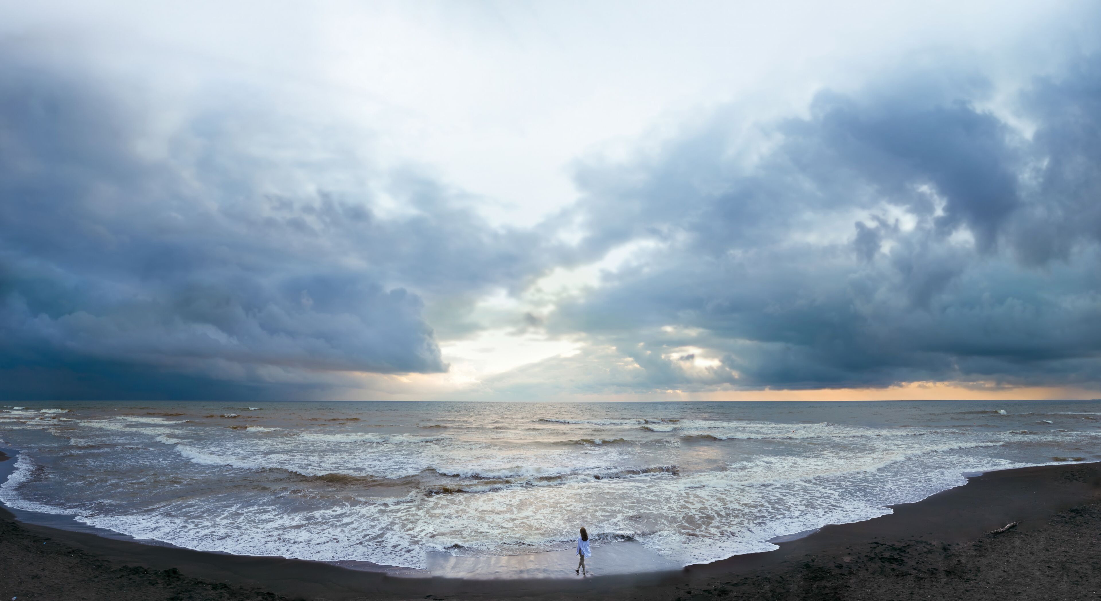 Aerial view of a young woman standing on a black beach on the surf line. summer day, rainy clouds. Sunset. Coast of Ureki beach, Georgia