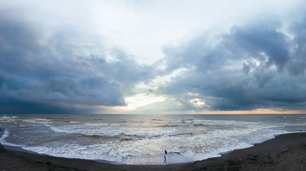 Aerial view of a young woman standing on a black beach on the surf line. summer day, rainy clouds. Sunset. Coast of Ureki beach, Georgia