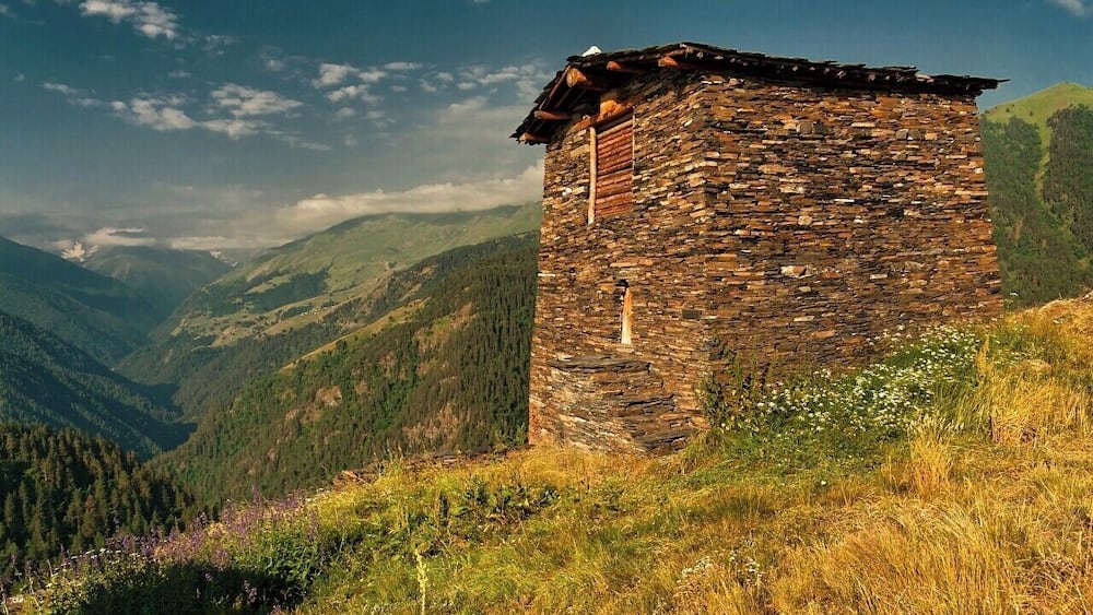 A stone tower on a hillside with a mountainous backdrop.