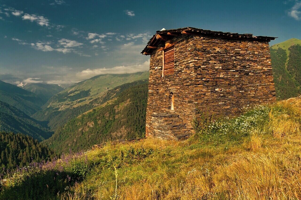 A stone tower on a hillside with a mountainous backdrop.