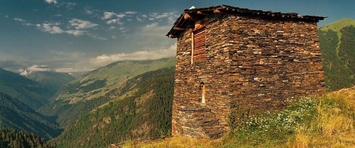 A stone tower on a hillside with a mountainous backdrop.
