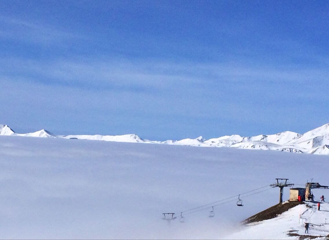 Paisaje montañoso nevado con un telesilla y un cielo azul despejado.