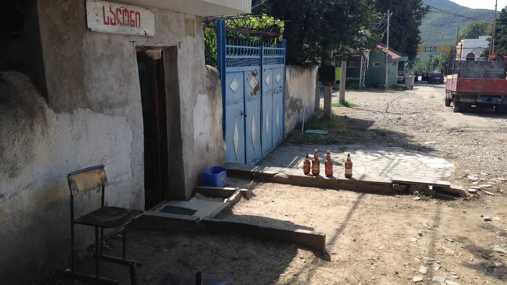 A building with a sign, a blue gate, and a dirt road with bottles.