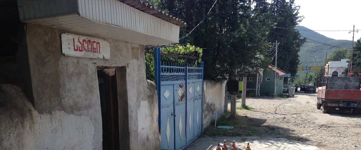 A building with a sign, a blue gate, and a dirt road with bottles.