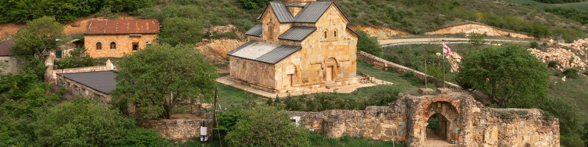 A historic church with a bell tower, surrounded by lush green hills and a stone archway.