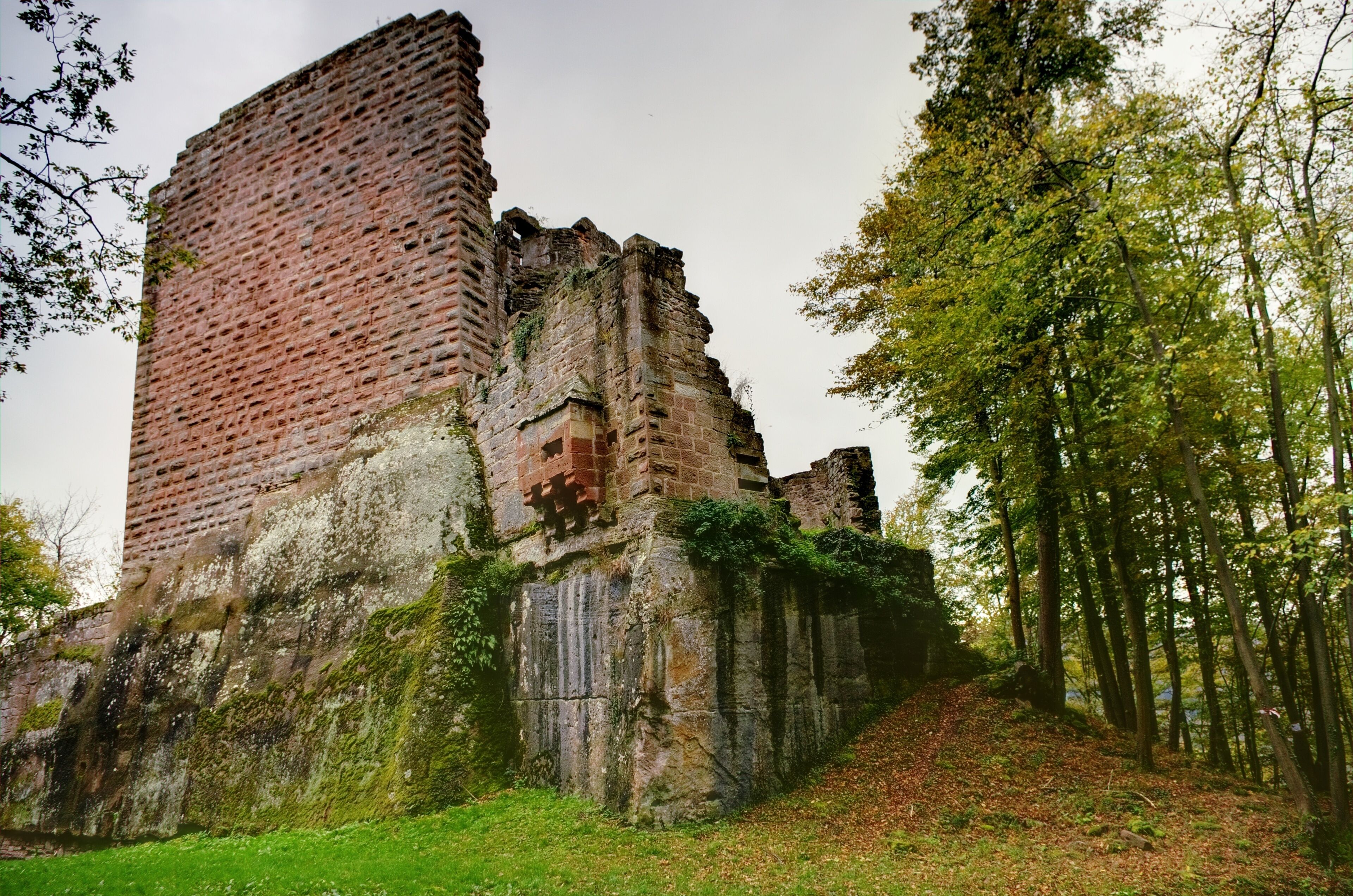 A historic brick ruin with overgrown vegetation and a forested hillside.