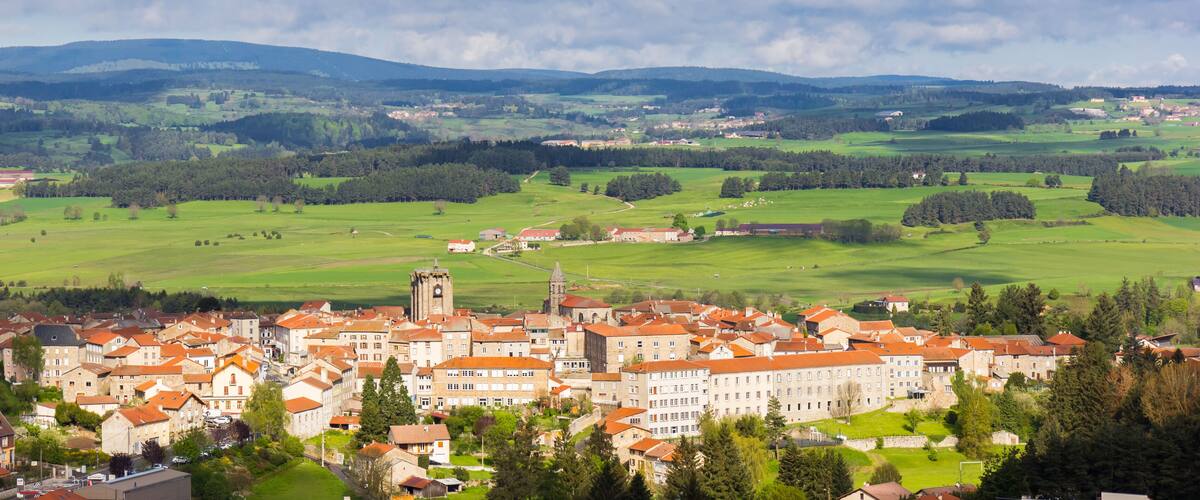 A town with red-roofed buildings, a prominent church tower, and rolling green hills in the background.