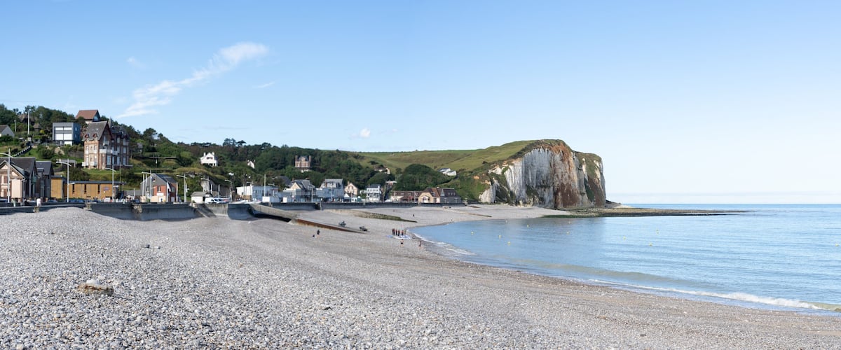 A pebble beach with houses and cliffs.