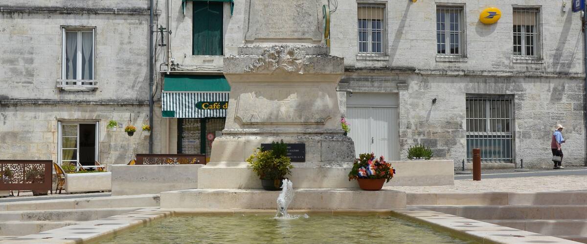 A fountain with a statue in the center, surrounded by a square with buildings in the background.