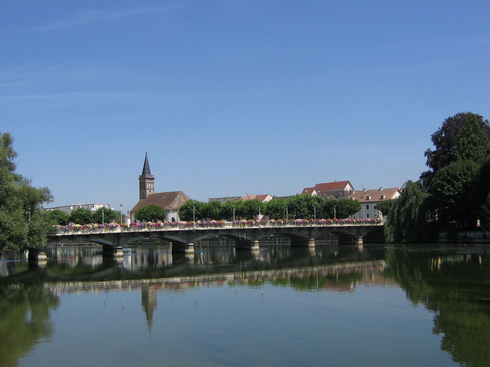 A bridge over a calm river with a church tower in the background.