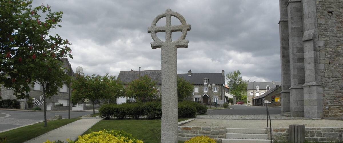 A stone cross in a courtyard with a stone building in the background.