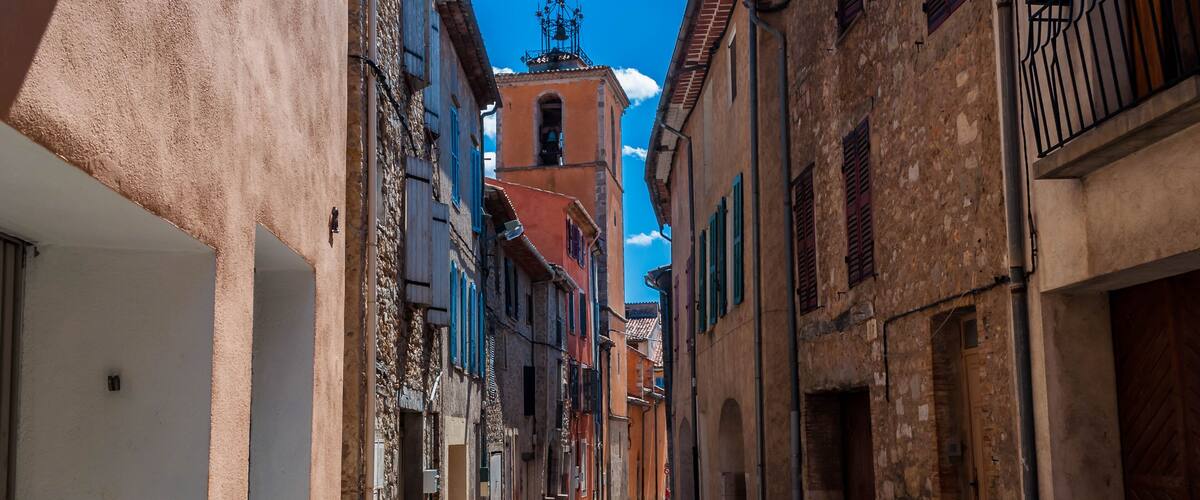 A narrow street flanked by historic buildings with a prominent bell tower in the distance.