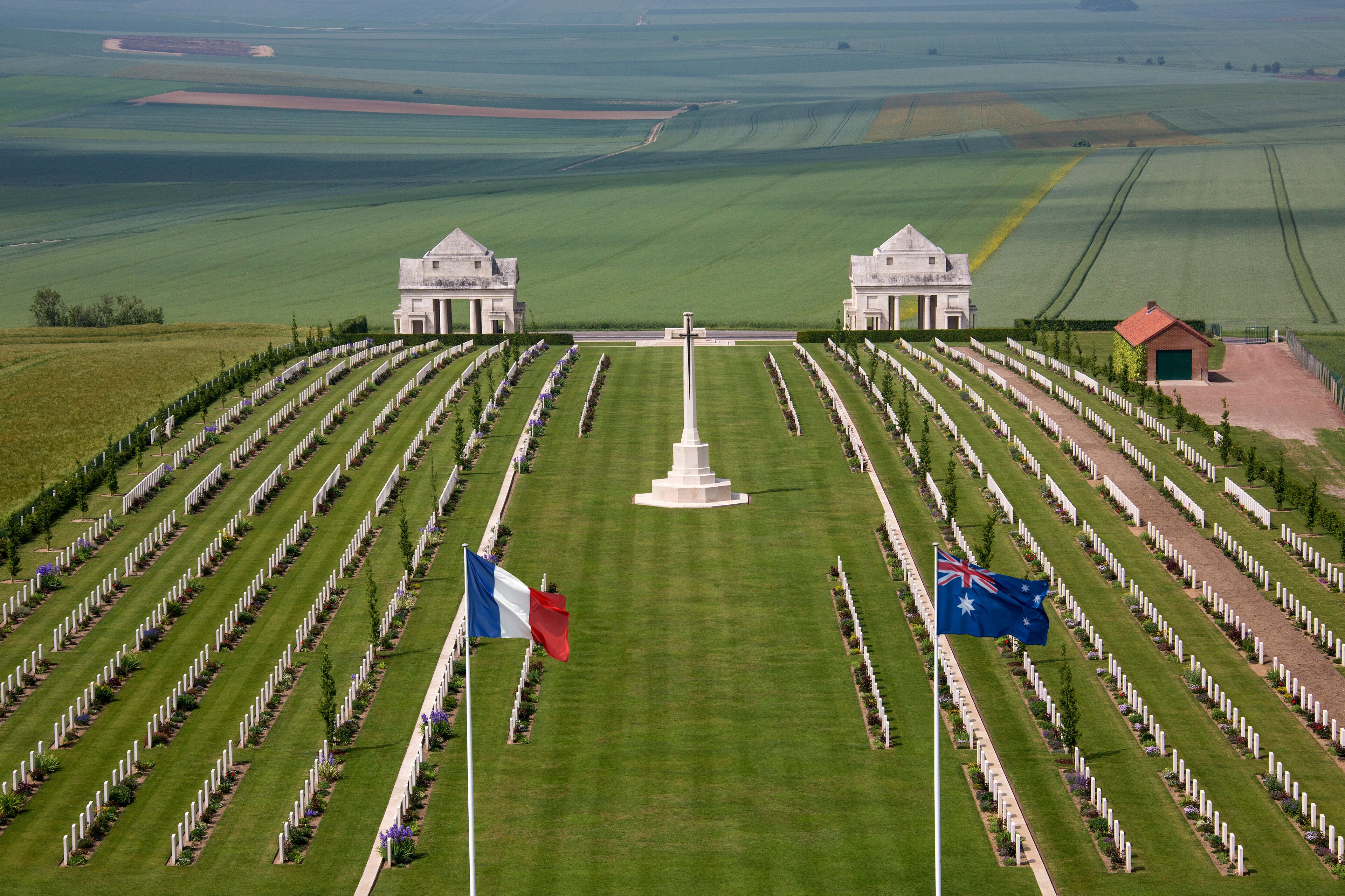 A cemetery with rows of graves, a central monument, and two buildings.