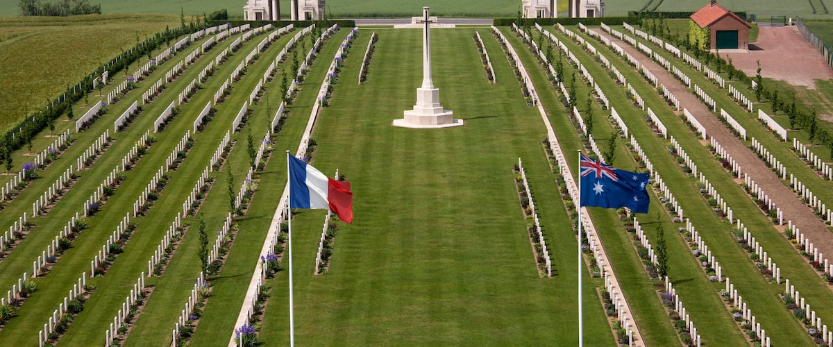 A cemetery with rows of graves, a central monument, and two buildings.