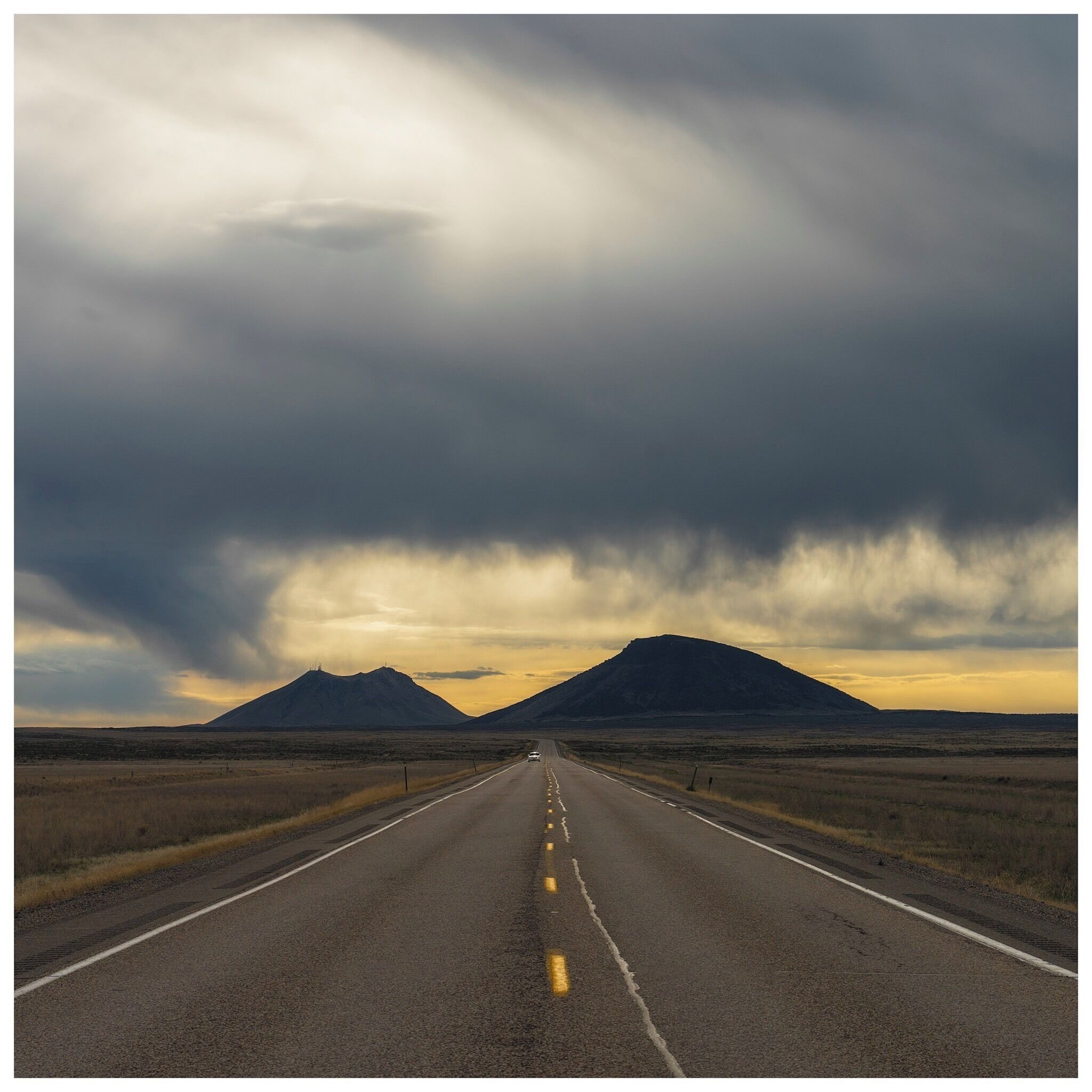 A road leading to two mountains under a cloudy sky.