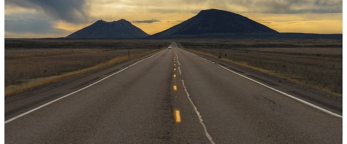 A road leading to two mountains under a cloudy sky.