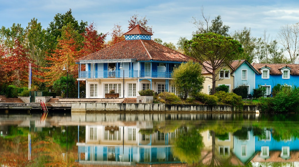 A blue house with a tiled roof, a pond reflecting the building, and autumn-colored trees in the background.
