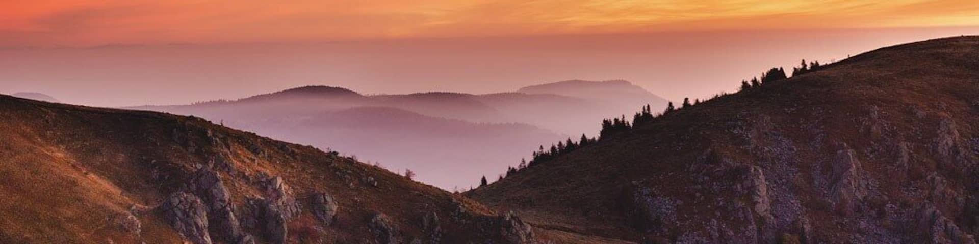 A mountainous landscape with rolling hills and a sunset sky.