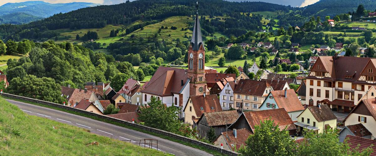 A picturesque village with a prominent church tower, surrounded by lush green hills and traditional houses.