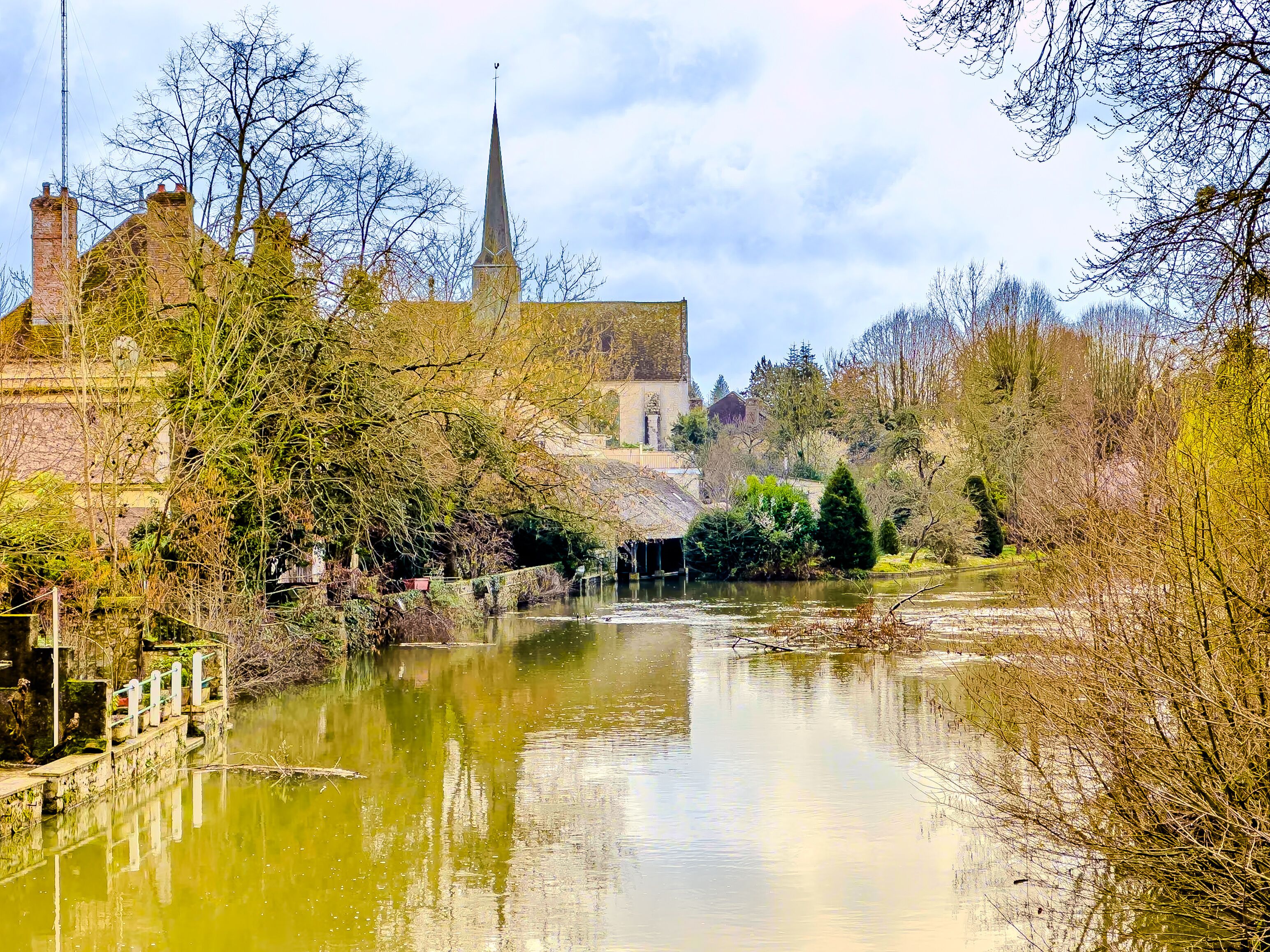 A river with a bridge, a church with a spire, and surrounding trees.