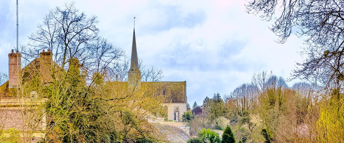 A river with a bridge, a church with a spire, and surrounding trees.