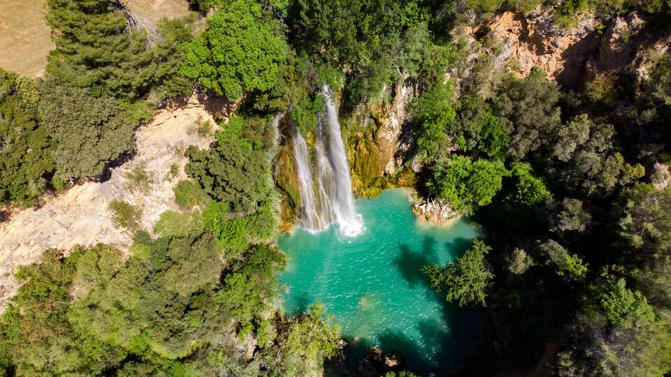 A waterfall cascading into a turquoise pool surrounded by dense forest.