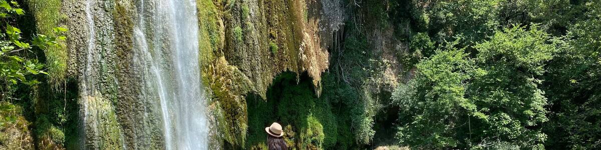 Ein Wasserfall stürzt in ein klares, türkisfarbenes Becken, umgeben von felsigem Gelände und üppiger Vegetation.
