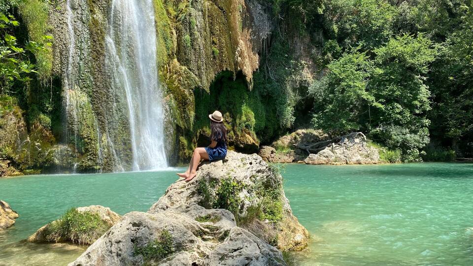 A waterfall cascading into a clear turquoise pool surrounded by rocky terrain and lush greenery.