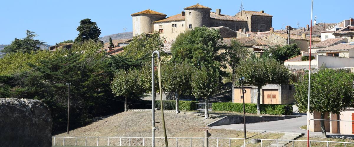 A historic castle with multiple towers, surrounded by trees and residential buildings.