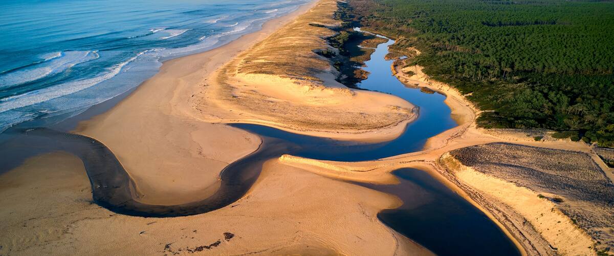 An aerial view of a coastal landscape with a sandy beach, a river, and a forested area.