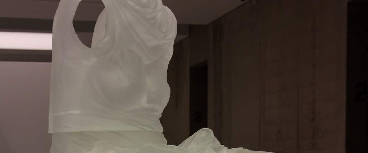 A modern sculpture of a figure in white, seated on a white pedestal.