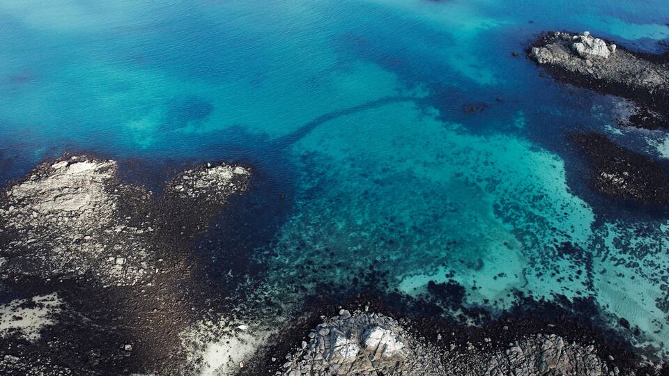 A coastal landscape with clear turquoise waters, rocky outcrops, and a small boat in the distance.