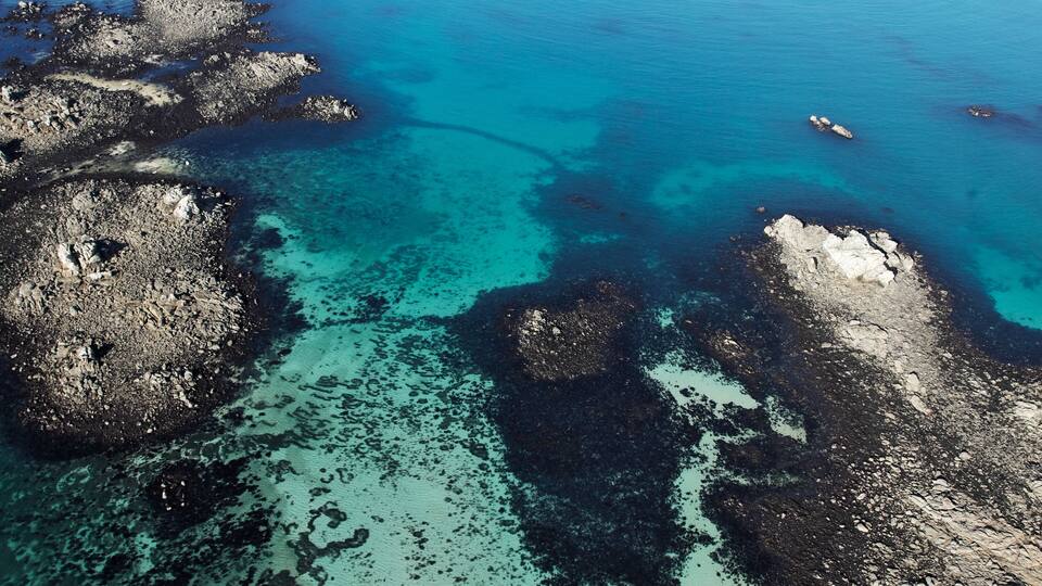 A coastal landscape with clear turquoise waters, rocky formations, and a small boat in the distance.
