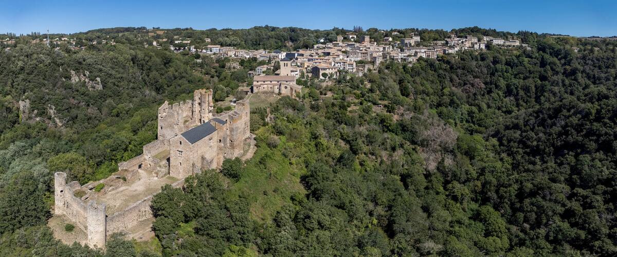 A medieval castle on a hillside with a village in the background.