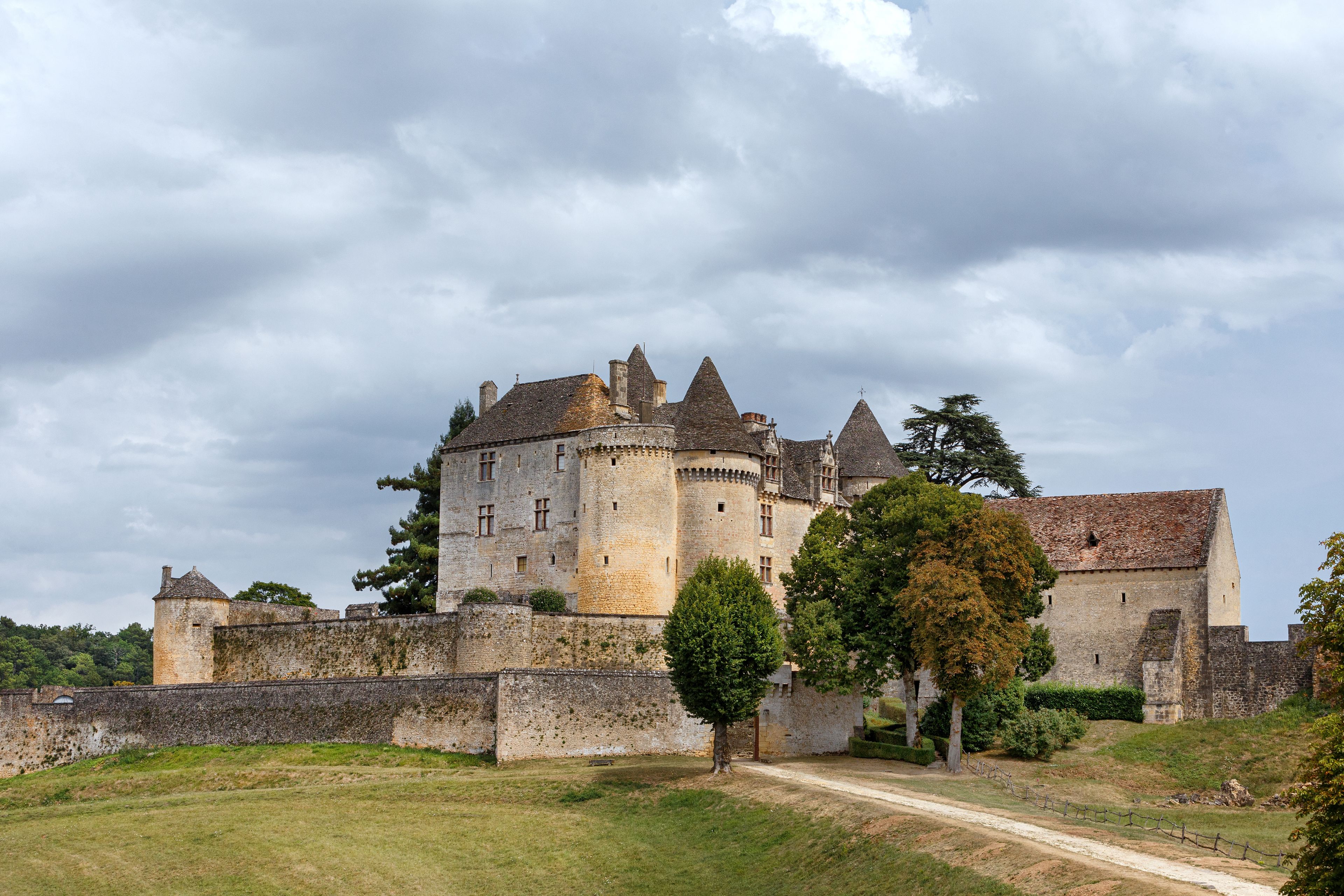 A historic castle with a moat, surrounded by greenery and a cloudy sky.