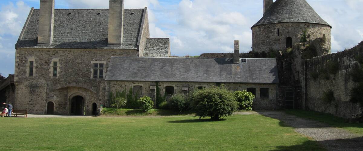 A historic stone building with a large courtyard, a round tower, and a grassy lawn.