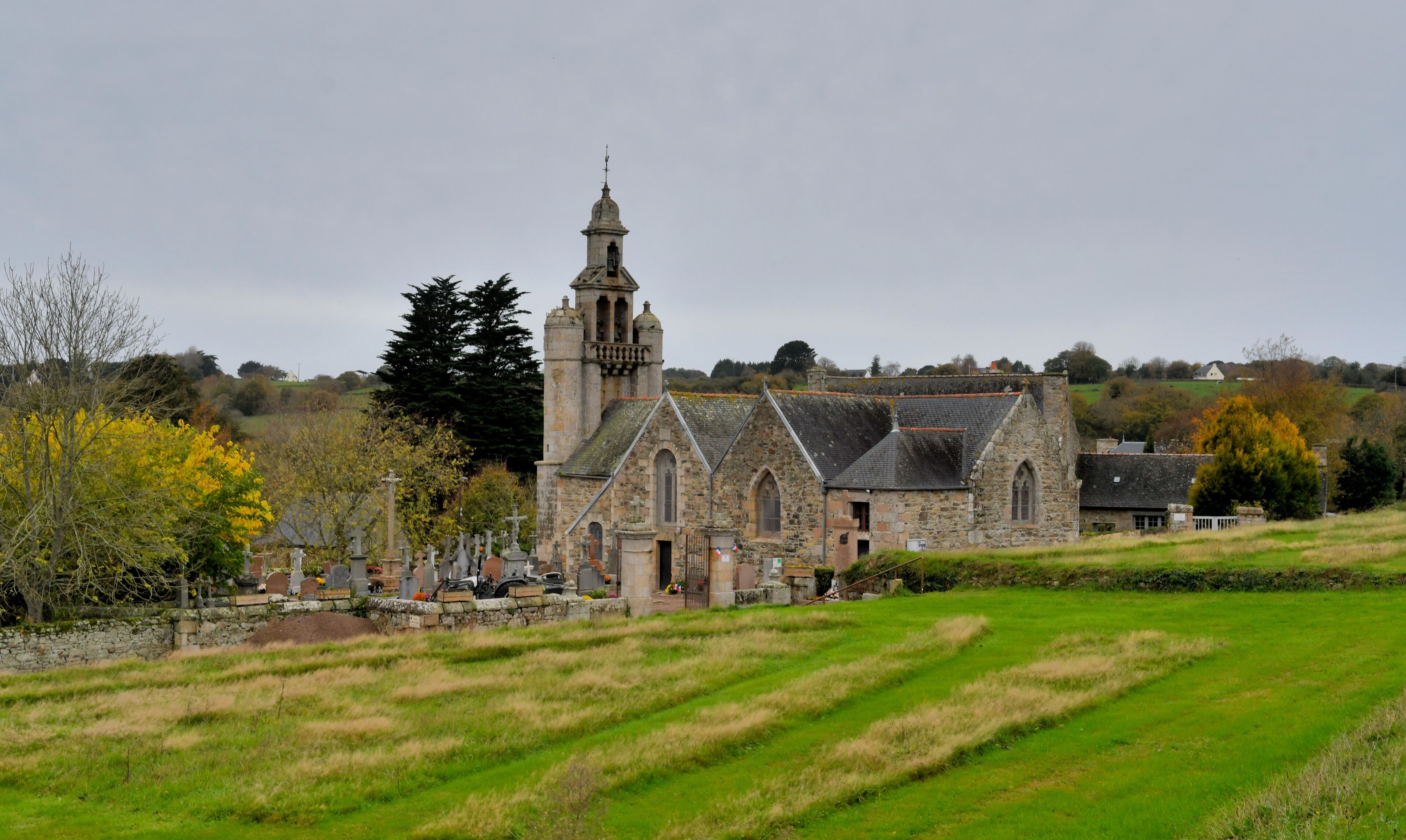 A historic stone church with a tall bell tower, surrounded by a cemetery and fields.