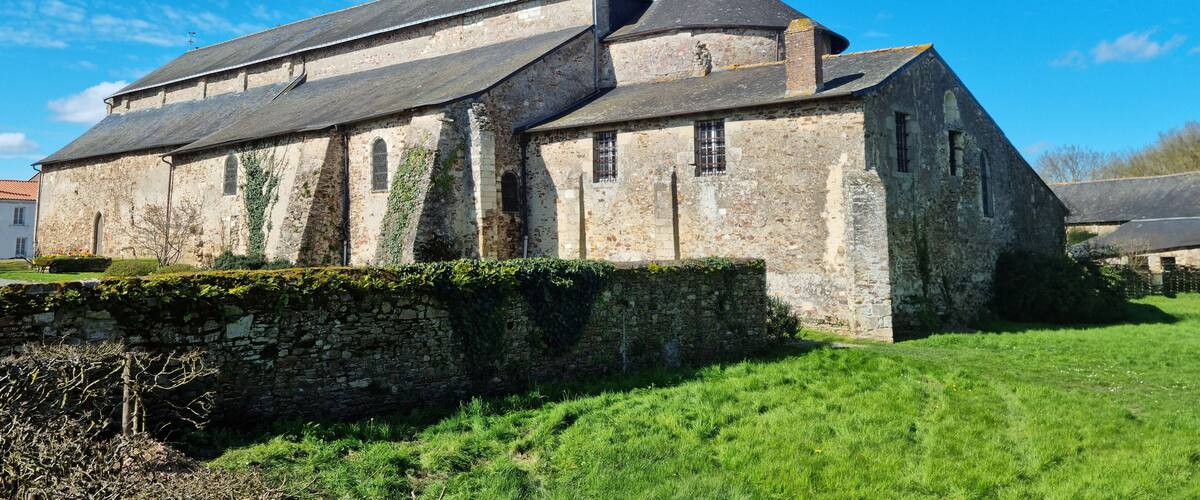 A historic stone building with a sloped roof and ivy growth, surrounded by a grassy area and a stone wall.