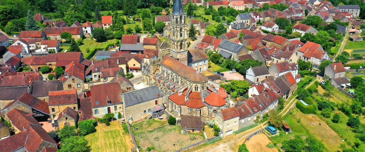 An aerial view of a historic town with a prominent church, surrounded by residential buildings and lush greenery.
