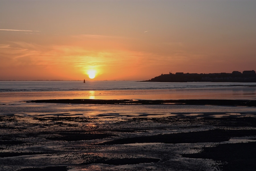 A sunset over a beach with calm waters and a distant shoreline.