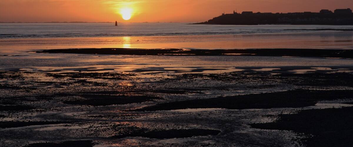A sunset over a beach with calm waters and a distant shoreline.