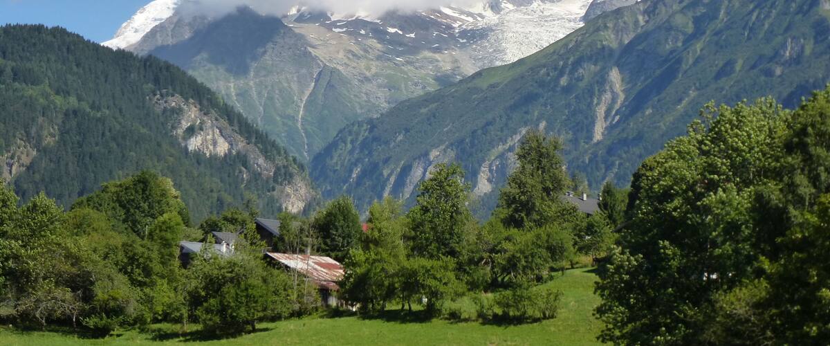 A mountainous landscape with snow-capped peaks, a valley with green fields, and a small house with a red roof.