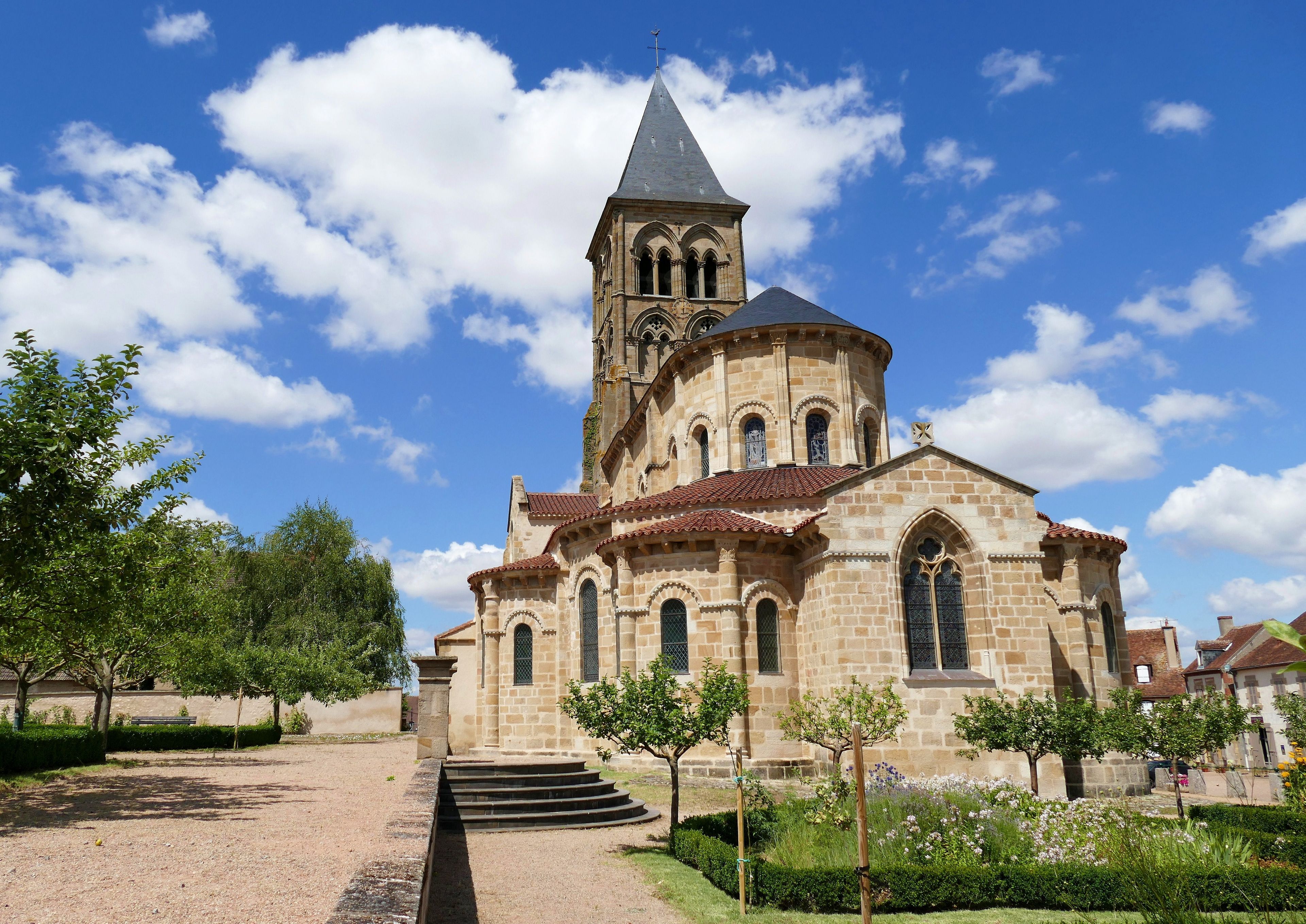 A historic church with a bell tower, surrounded by a well-maintained garden and a clear blue sky.