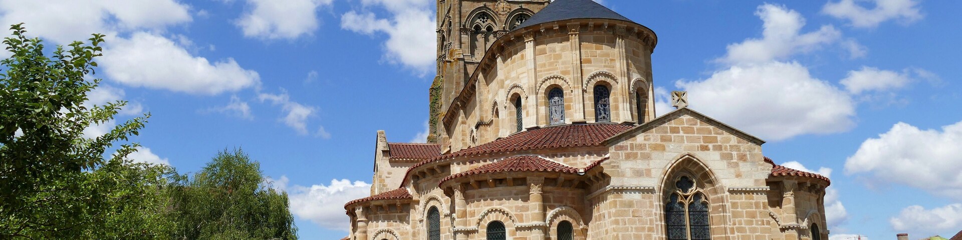 Una iglesia histórica con un campanario, rodeada por un jardín bien cuidado y un cielo azul despejado.